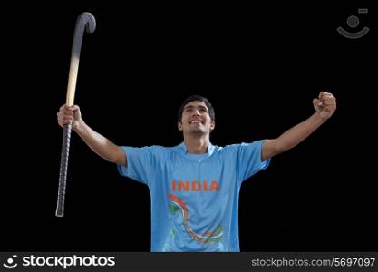 Happy young man with hockey stick celebrating victory isolated over black background