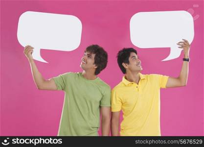 Happy young men holding speech bubbles over pink background