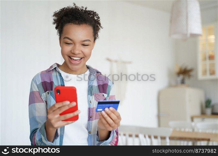 Happy young mixed race girl holding bank credit card and phone, laughing feeling excited of fast money transfer, high cashback after purchasing, using online banking services app at home. E-banking.. Mixed race girl holds credit card, phone, happy with high cashback using online banking services