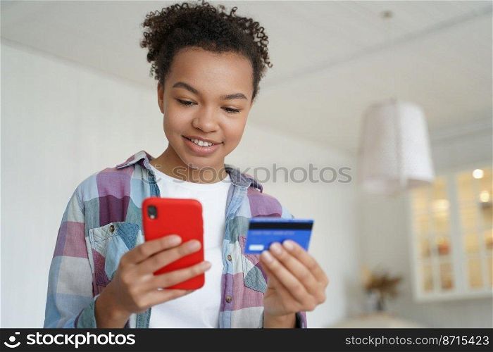 Happy young mixed race girl holding credit card and smartphone, transferring money, shopping in internet store. Modern teen lady using mobile bank app, online banking services, standing at home.. Happy teen mixed race girl holding credit card, phone, uses mobile bank app, online banking services