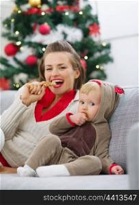 Happy young mother and baby eating cookies near Christmas tree