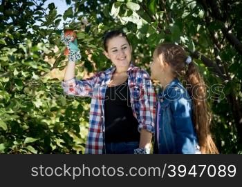Happy young mother and daughter picking apples from tree at garden