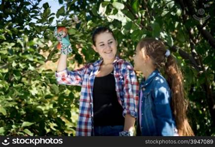 Happy young mother and daughter picking apples from tree at garden