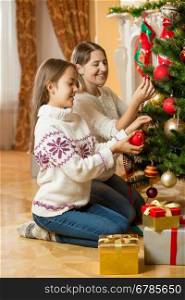 Happy young mother and daughter sitting on floor at living room and decorating Christmas tree