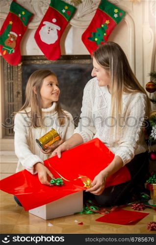 Happy young mother and daughter wrapping Christmas presents and looking at each other