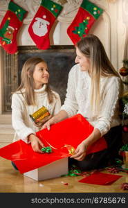 Happy young mother and daughter wrapping Christmas presents and looking at each other