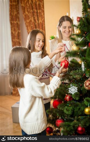Happy young mother and two daughters decorating Christmas tree with baubles