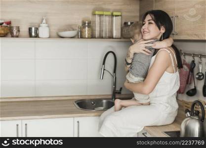 happy young mother carrying her son sitting kitchen counter