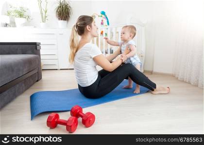 Happy young mother doing yoga with her baby boy on floor at living room
