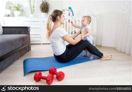 Happy young mother exercising on floor with her baby boy