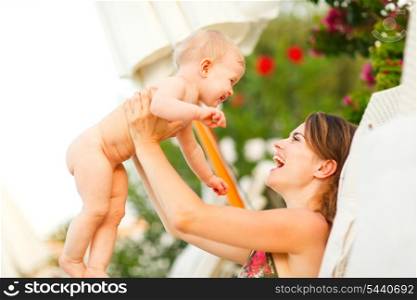 Happy young mother laying on sunbed and playing with baby
