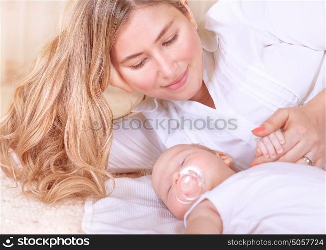 Happy young mother lying down with cute newborn baby at home, enjoying first days of parenthood, tender loving family, new life concept