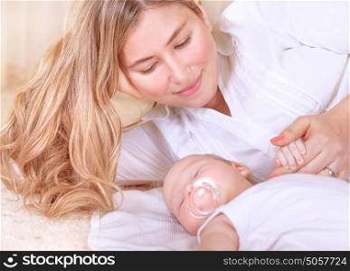 Happy young mother lying down with cute newborn baby at home, enjoying first days of parenthood, tender loving family, new life concept