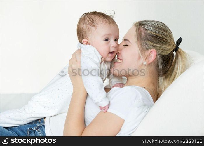 Happy young mother lying on bed and holding her 3 months old baby boy
