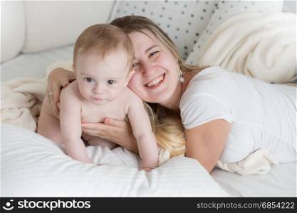 Happy young mother lying on big pillow with her 9 months old baby