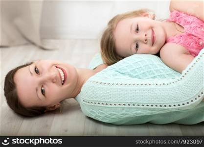 Happy young mother lying on the floor and holding smiling little daughter on the chest. Smiling mother and daughter on the floor