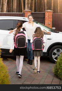 Happy young mother meeting her two daughters after school at car