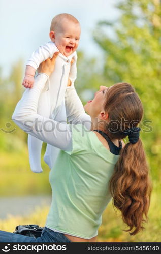 Happy young mother playing with laughing baby girl in park&#xA;