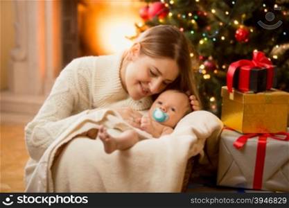 Happy young mother posing with newborn son under Christmas tree