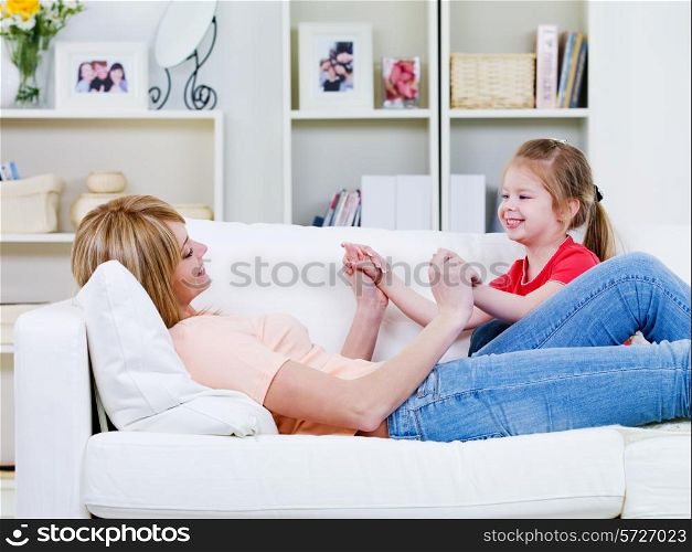Happy young mother relaxing on the sofa and playing with her little daughter - indoors
