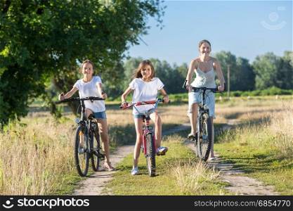 Happy young mother riding on bicycles with two daughters