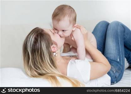 Happy young mother sitting on bed and holding her 9 months old baby boy