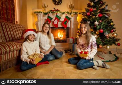 Happy young mother sitting with two daughters on floor next to burning fireplace