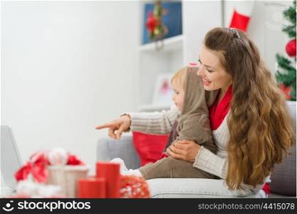 Happy young mother spending Christmas with baby and pointing on laptop