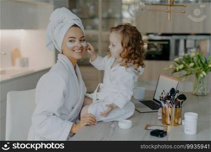 Happy young mother teacher her little daughter to do makeup. Culry small girl applies beauty patches under eyes to mom use beauty products naturl cosmetics. Skin care and family time concept