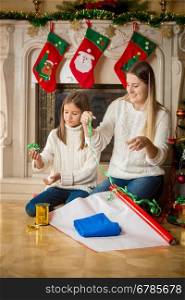 Happy young mother teaching her daughter how to wrap Christmas presents