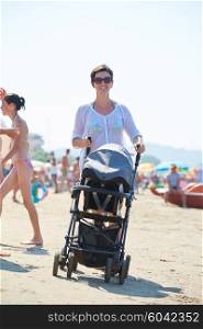 happy young mother walking on beach and push baby carriage