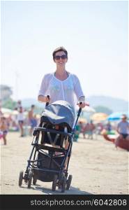 happy young mother walking on beach and push baby carriage