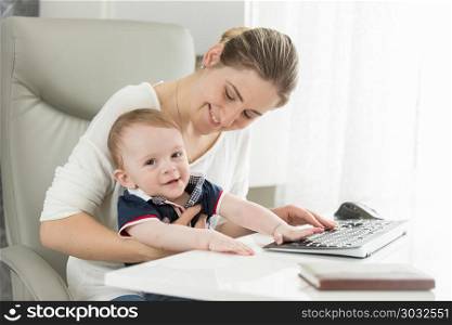 Happy young mother with baby son sitting behind desk at home office. Happy mother with baby son sitting behind desk at home office