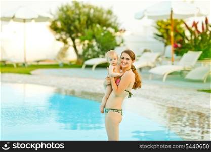 Happy young mother with cute baby standing in swimming pool