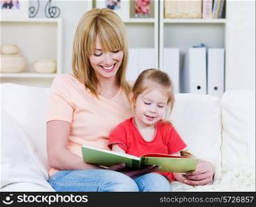 Happy young mother with her little smiling daughter reading the bood together - indoors