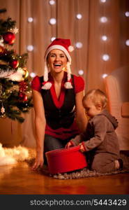 Happy young mother with lovely baby opening present box near Christmas tree&#xA;