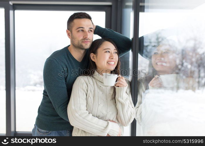 happy young multiethnic couple enjoying morning coffee by the window on cold winter day at home