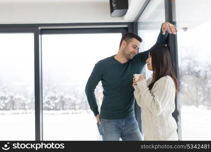 happy young multiethnic couple enjoying morning coffee by the window on cold winter day at home