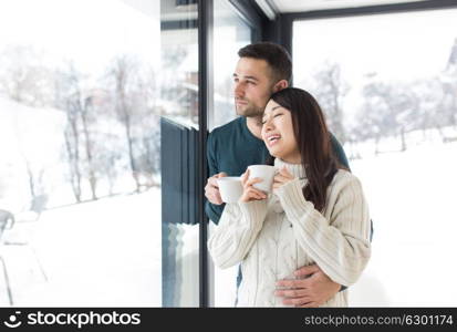 happy young multiethnic couple enjoying morning coffee by the window on cold winter day at home