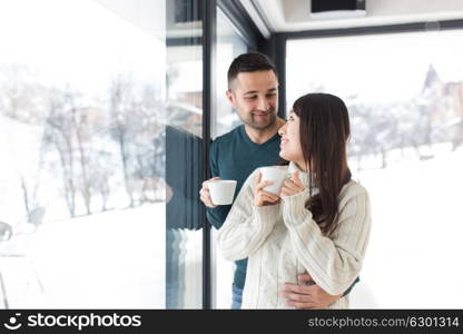 happy young multiethnic couple enjoying morning coffee by the window on cold winter day at home