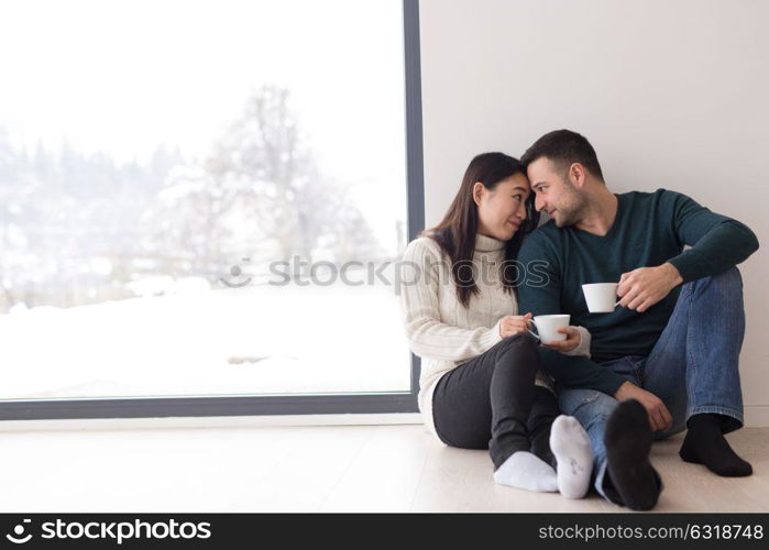 happy young multiethnic couple enjoying morning coffee by the window on cold winter day at home