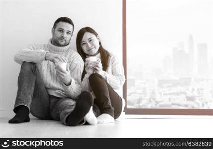 happy young multiethnic couple enjoying morning coffee by the window on cold winter day at home