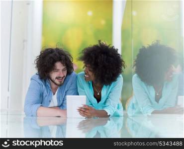 Happy young multiethnic couple lying on floor having fun using Digital Tablet