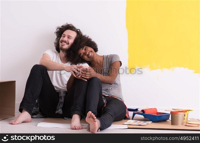 Happy young multiethnic couple relaxing after painting a room in their new house on the floor