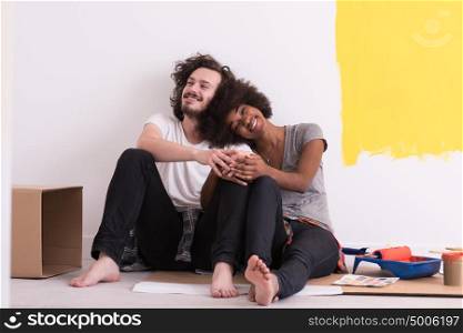 Happy young multiethnic couple relaxing after painting a room in their new house on the floor