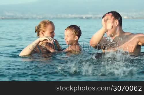 Happy young parents and little son fooling and splashing sea water. Family fun on summer vacation