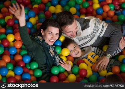 Happy young parents are playing with their kids at pool with colorful balls in a children&rsquo;s playroom