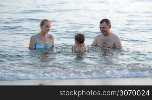 Happy young parents playing ball with a son in sea being close to shore
