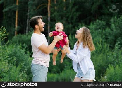Happy young parents with a baby are walking through the forest, having fun and enjoying happy moments