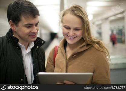 Happy young people at underground station. Woman holding tablet computer and they looking at screen while waiting for the train